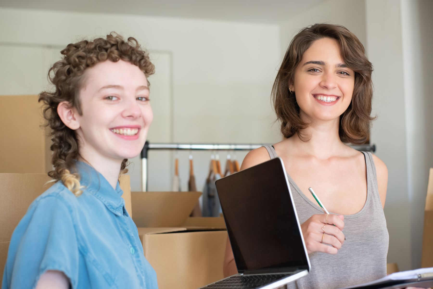 Twee collega's bekijken samen informatie op een laptop tussen dozen en werkmateriaal